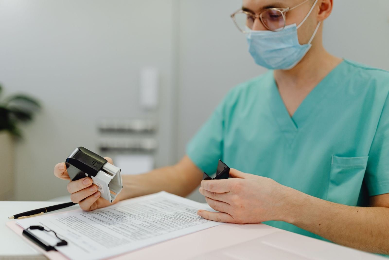 A medical professional in scrubs and a mask stamps a document at a desk