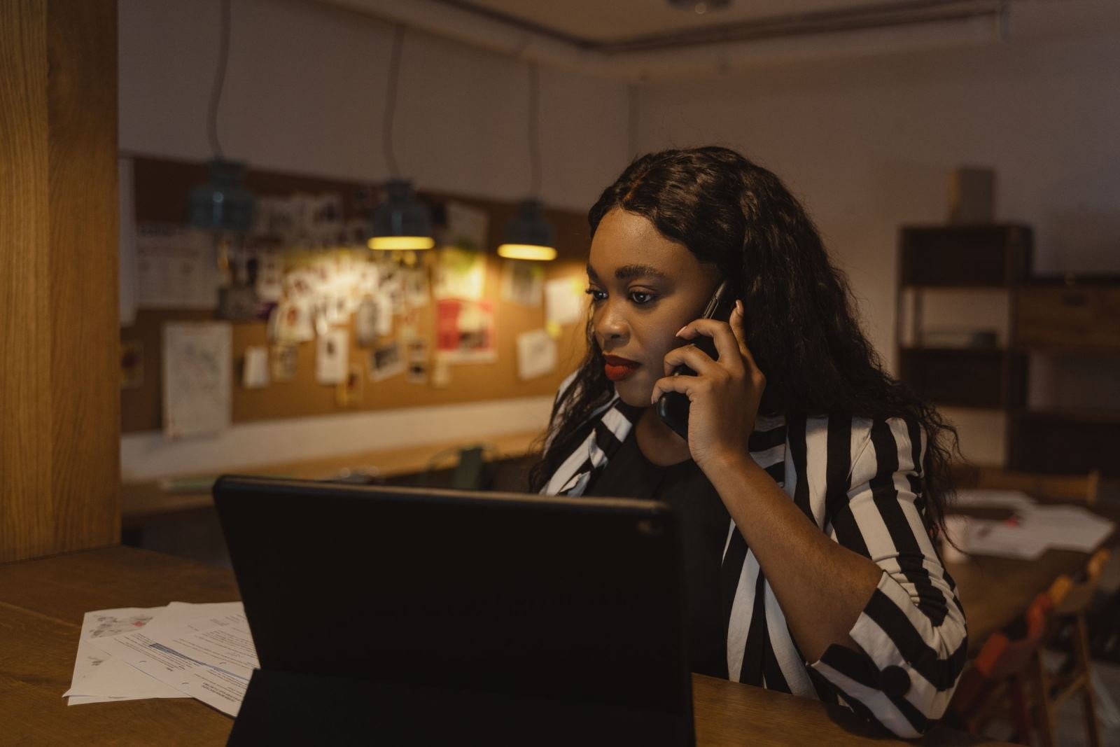 A woman sits at a desk and views a laptop while on a phone call