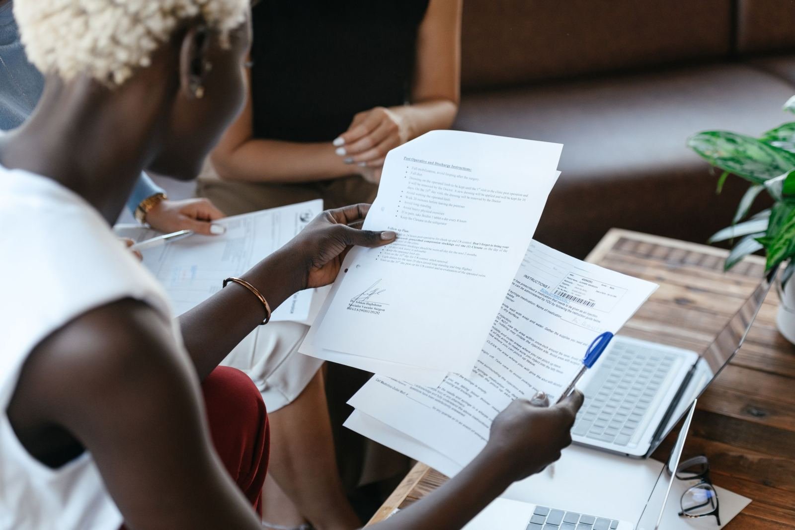 A woman sits at a desk with a laptop, checking papers.