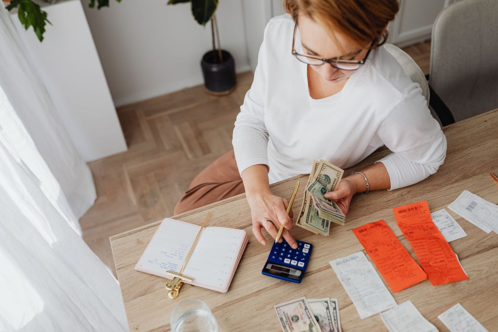 A woman uses a calculator and reviews receipts and cash at a wooden table