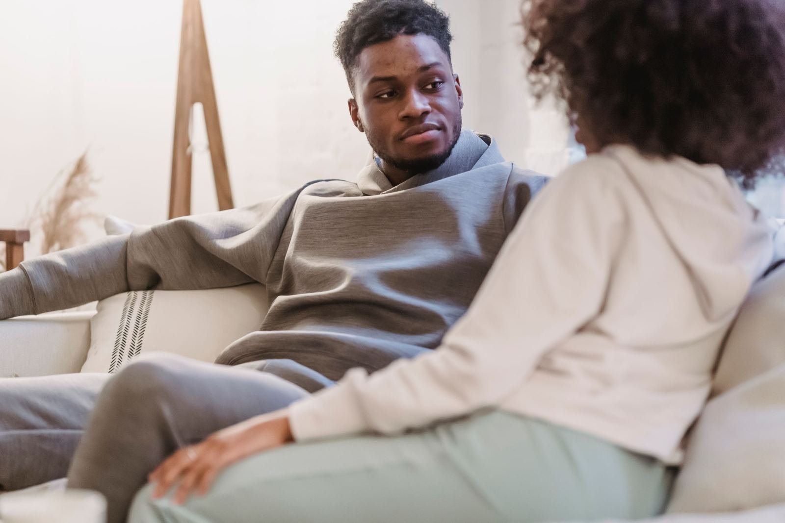A man and a woman are talking while seated on a white couch.