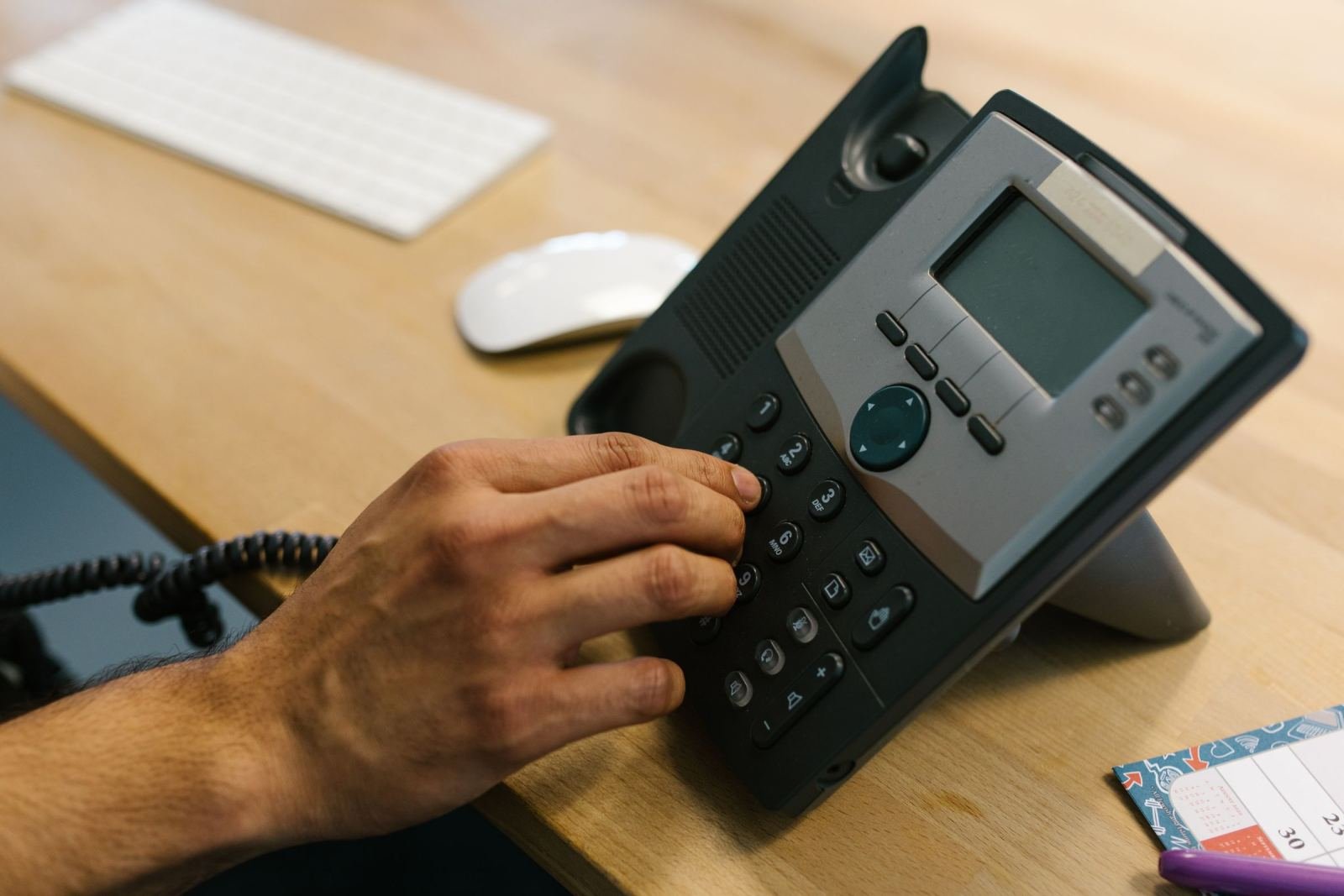 Image of a hand dialing a number on a black desk phone