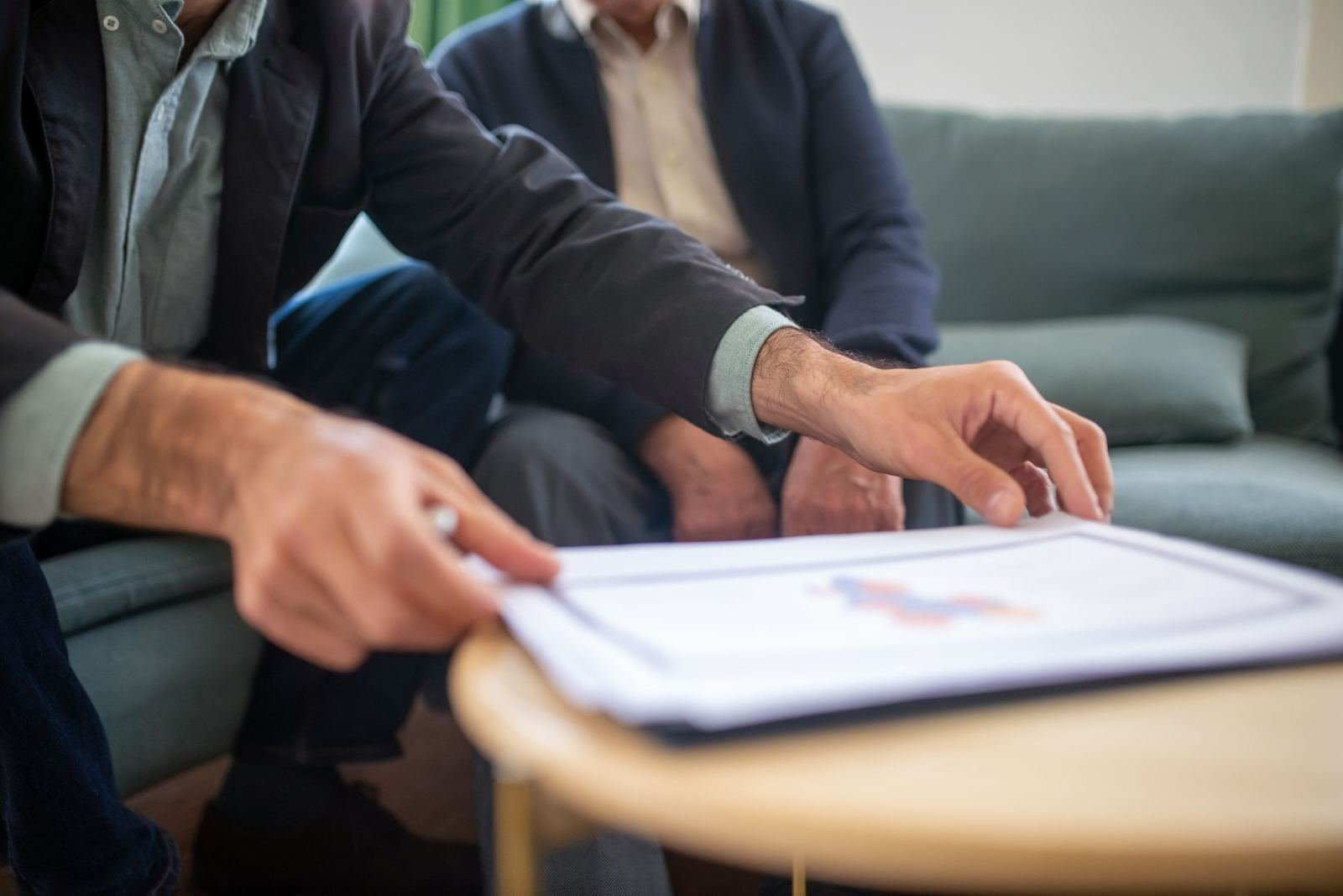 Two men review a document with a chart on a wooden table