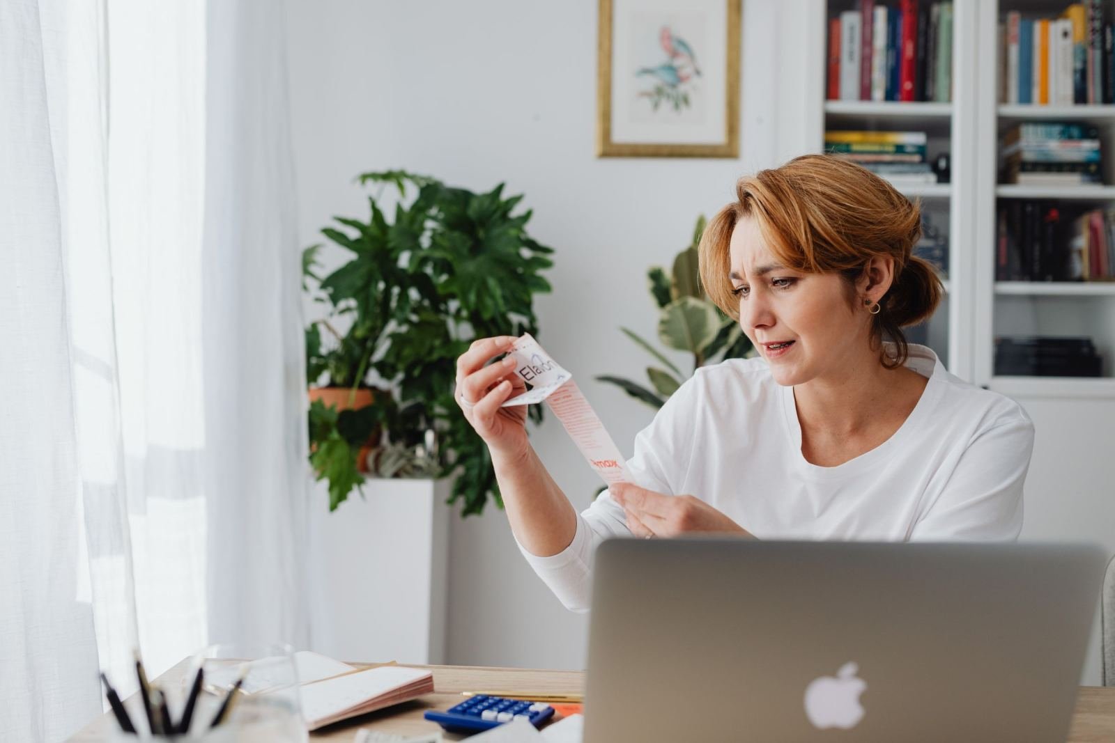 A woman looks at a receipt with a concerned expression while sitting at her laptop