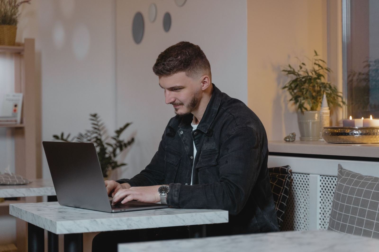 A man in a denim jacket uses a laptop at a white marble table