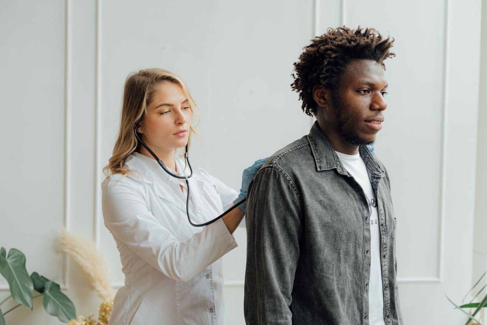 A doctor in a white coat uses a stethoscope to check a man's back.
