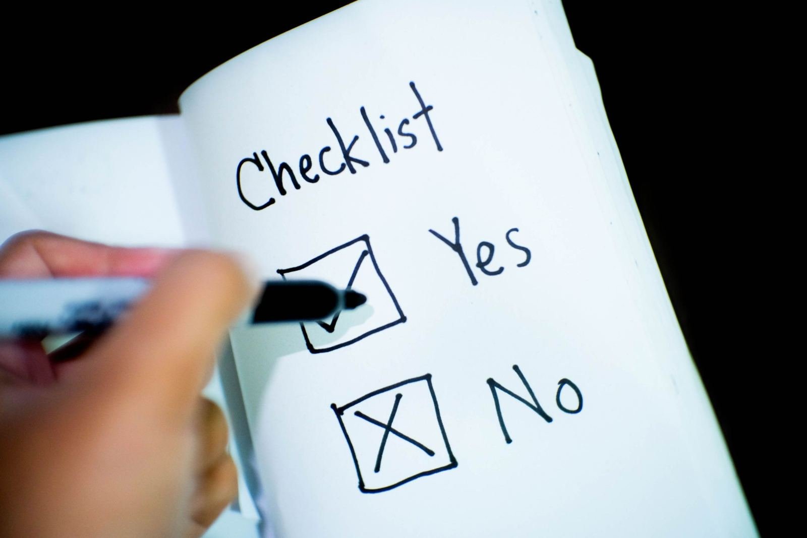 A hand holds a marker and checks a box marked 'Yes' on a handwritten list.