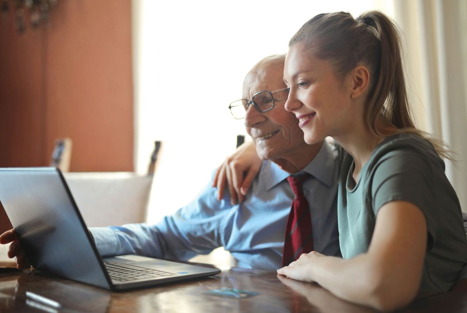 An older man and a younger woman smile while looking at a laptop together