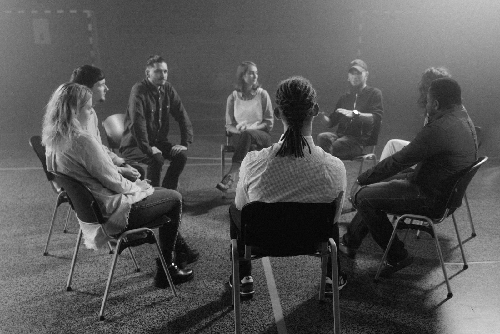 Six people sitting in a circle of chairs in a dim room