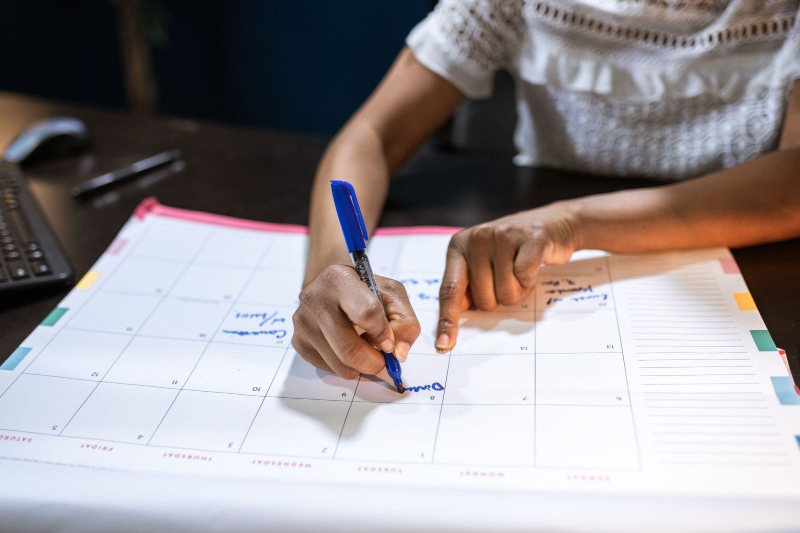 A person using a blue pen to mark a date on a large paper calendar