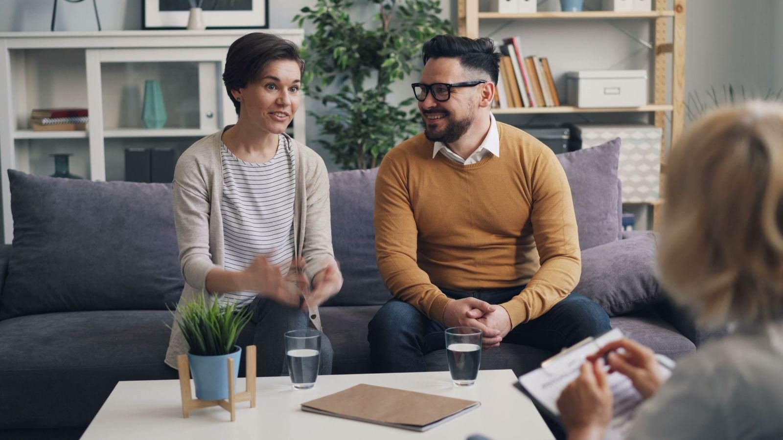 A couple sits on a sofa talking with a therapist in a modern office
