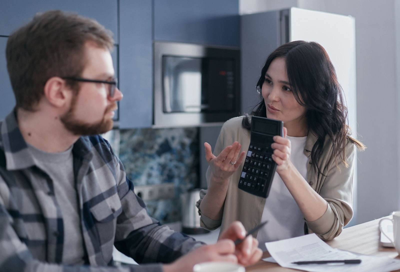A man and woman sit at a kitchen table reviewing paperwork with a calculator.