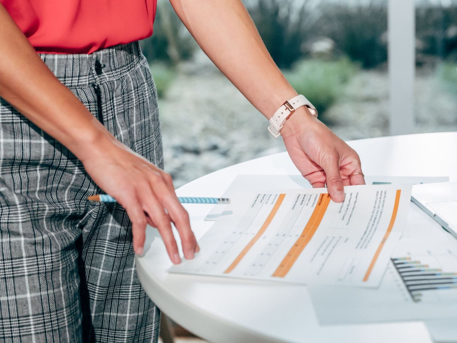 A person in plaid trousers reviews a highlighted document on a white table