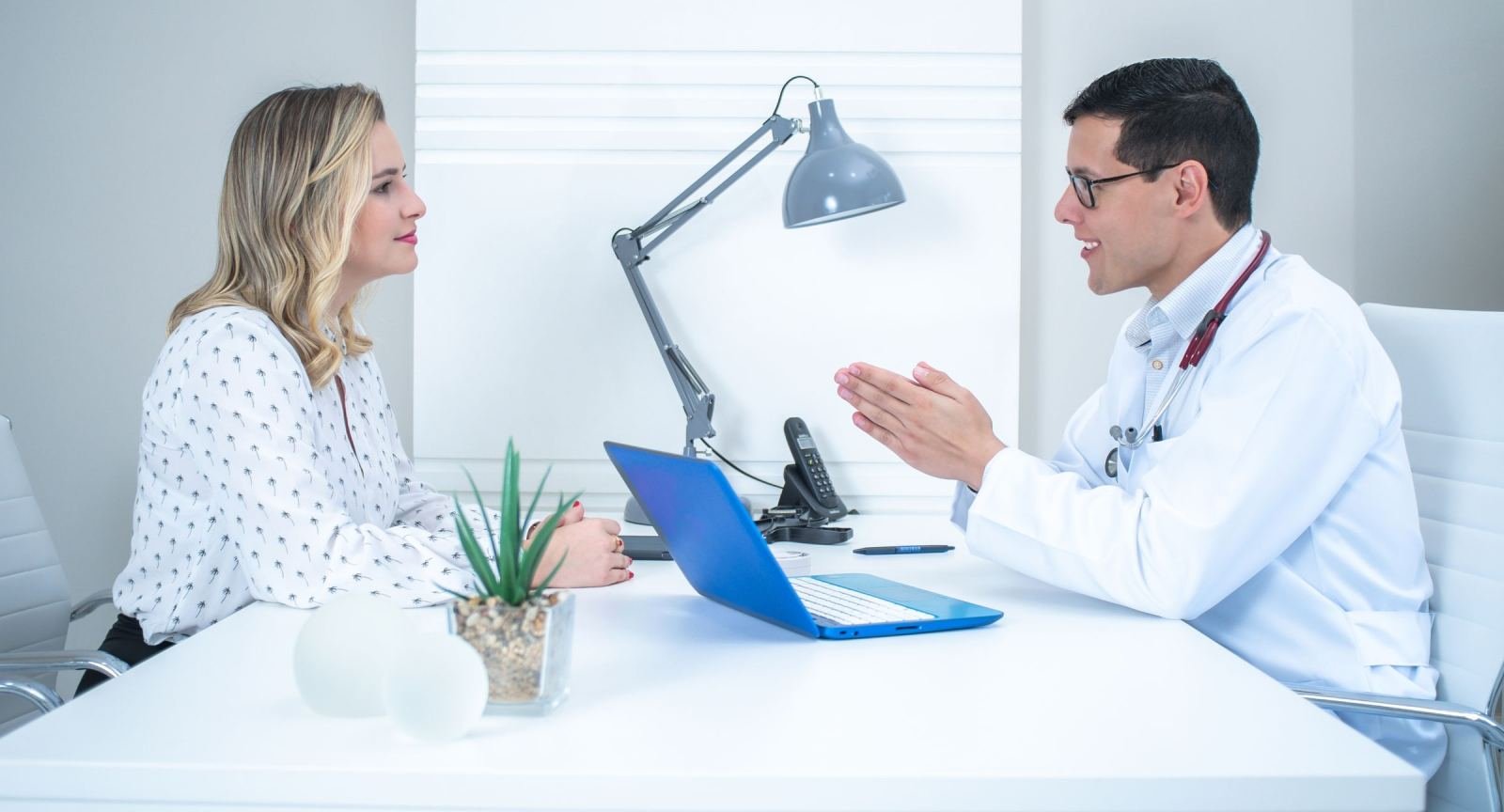 A woman speaks with a doctor in a white lab coat in a bright office