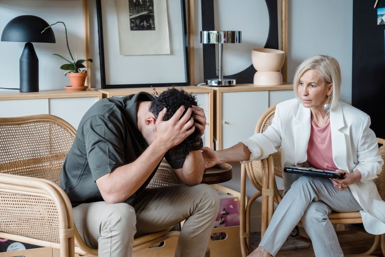 A therapist in a white blazer comforts a man sitting with his head in his hands