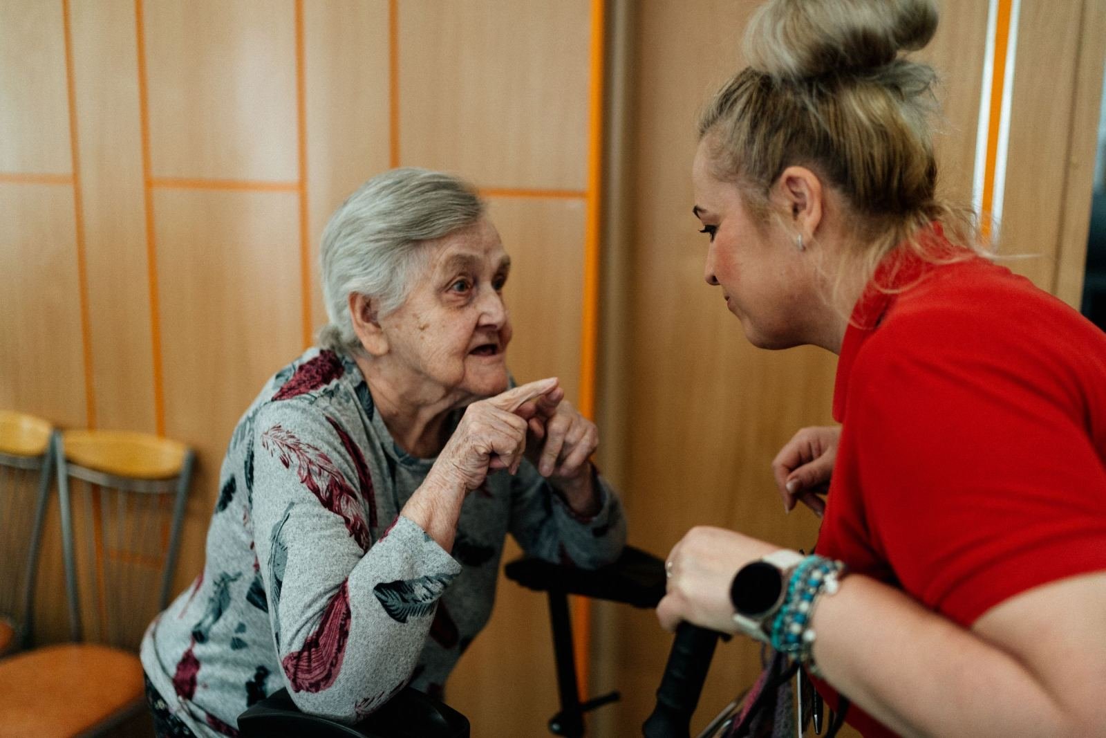 A senior woman with a walker talks to a staff member wearing a red shirt.