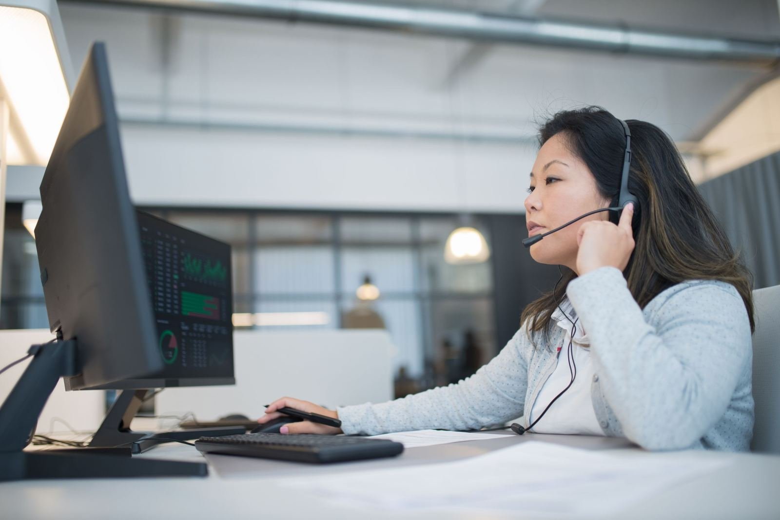 A woman in an office uses a headset while working on a computer