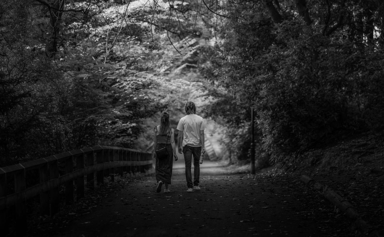 Two people walk side by side down a wooded path in a black and white photo