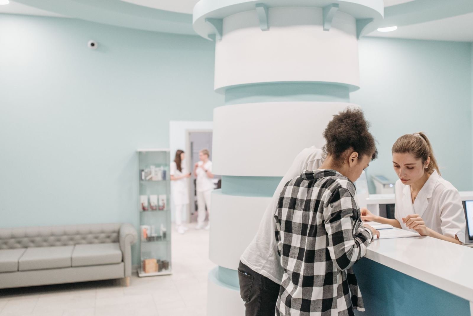 A medical staff member talks with two people at a clinic reception desk