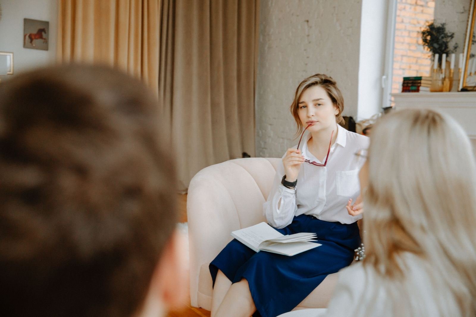 A woman in a white shirt sits in a chair and talks with two other people