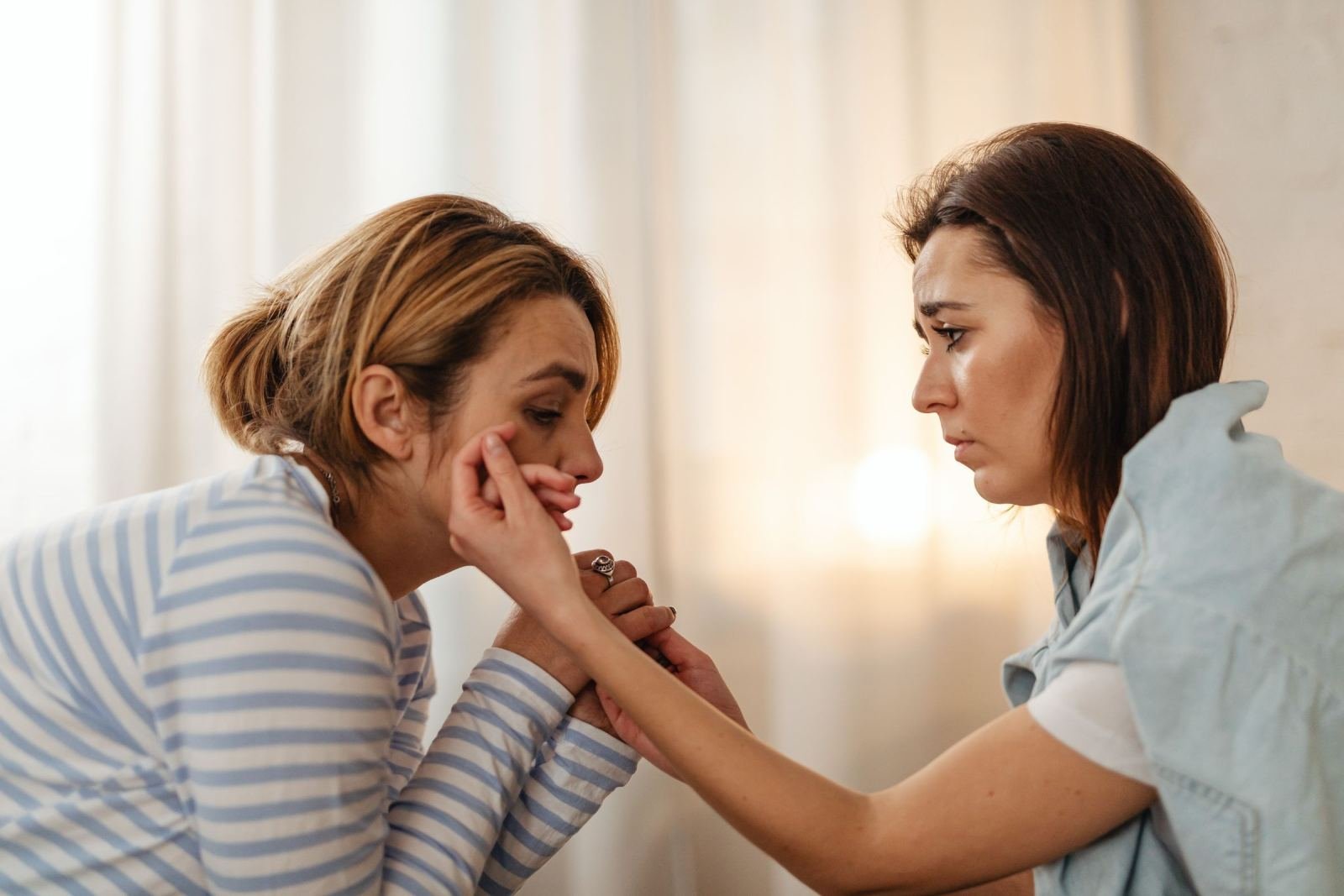 One woman reaches out to touch the cheek of another woman in a bright room
