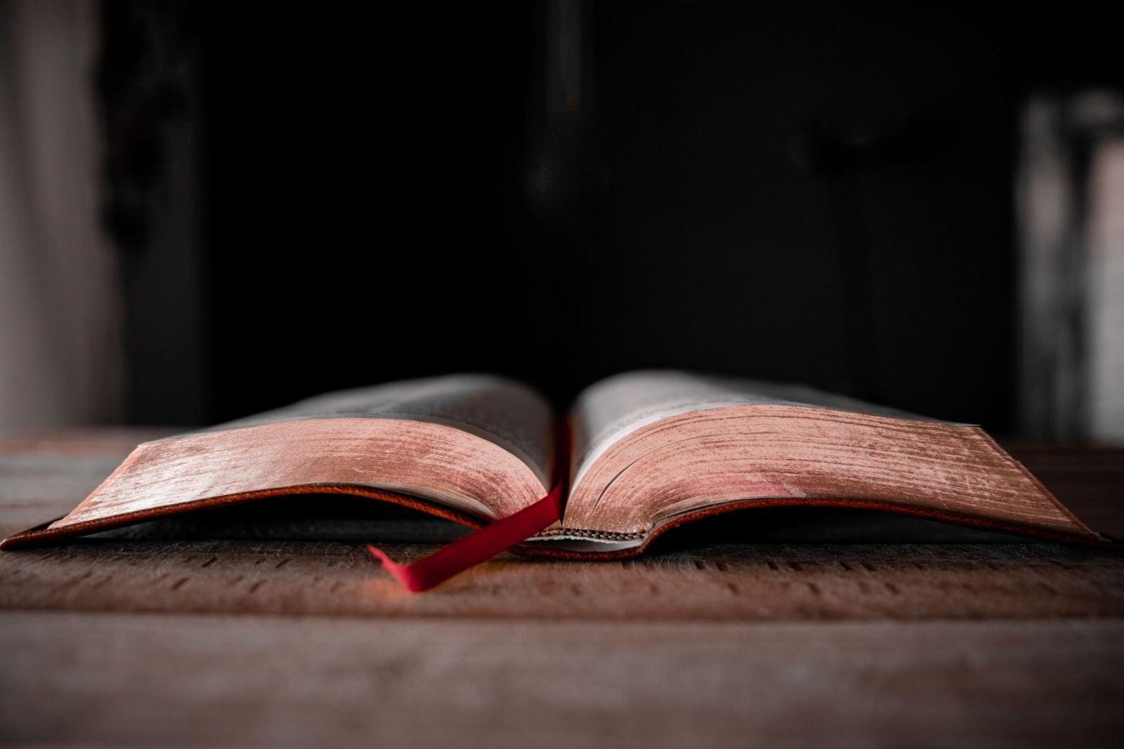 An open book with a red ribbon bookmark on a wooden surface
