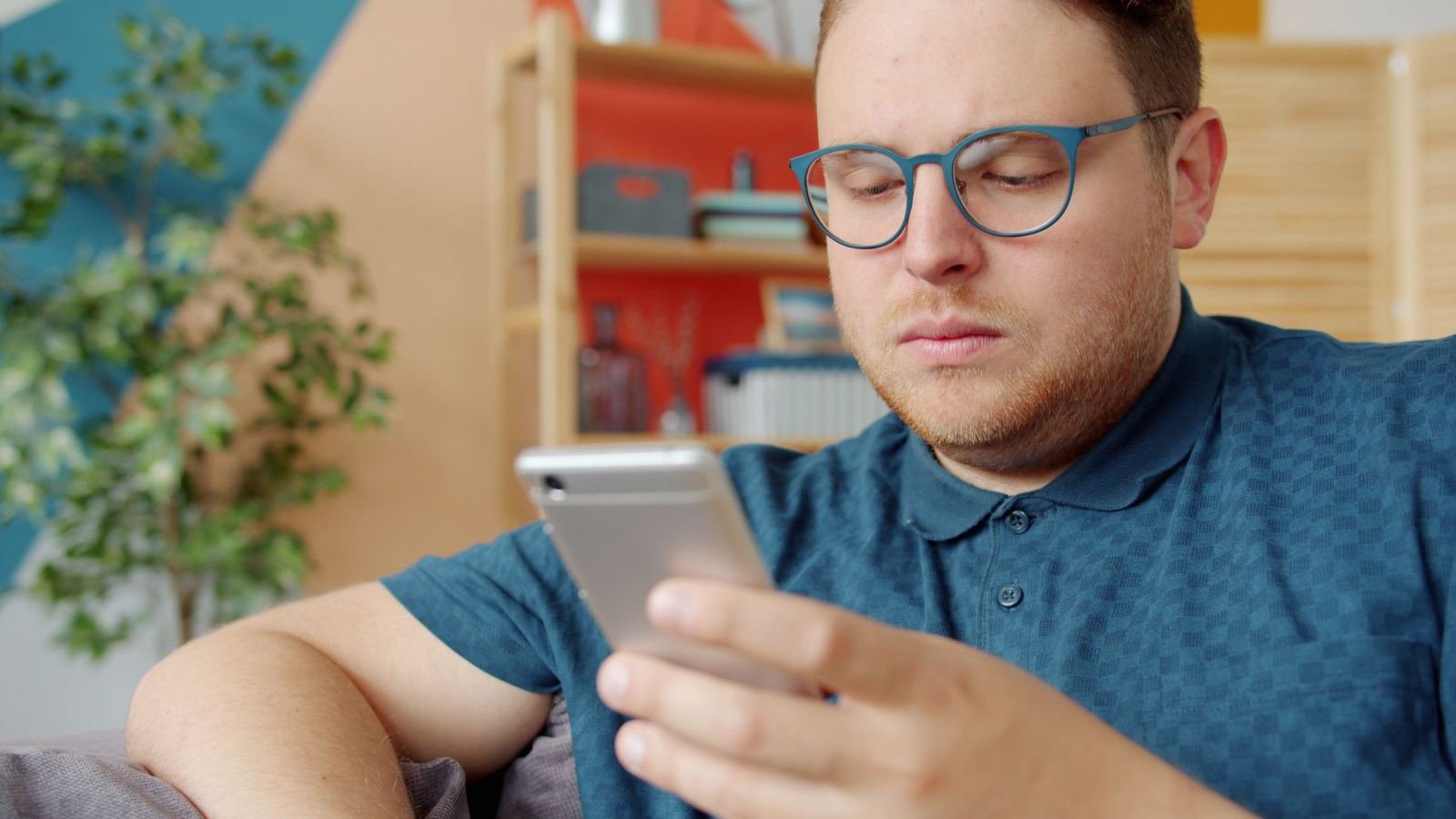 A man with glasses looks at his smartphone in a bright room