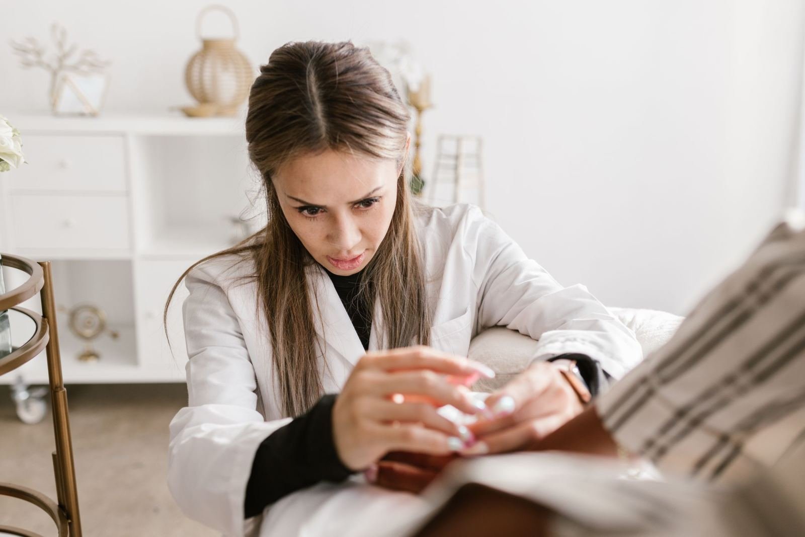 A doctor in a white coat holds a patient's hand in a bright room.