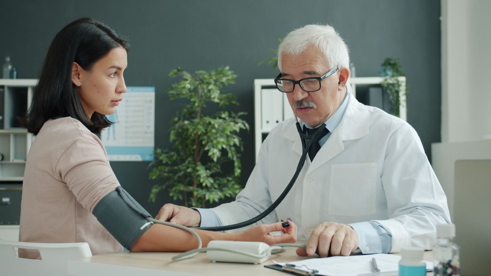 A doctor uses a blood pressure cuff on a patient's arm in a bright office