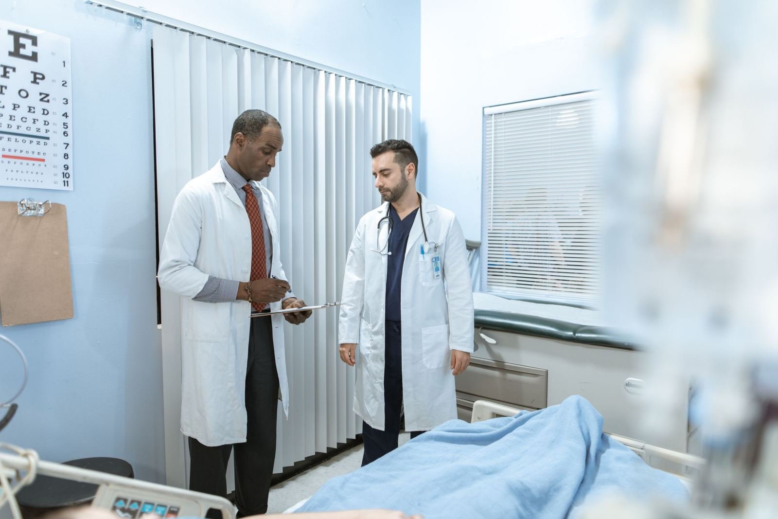 Two doctors in white coats discuss a patient's chart in an exam room