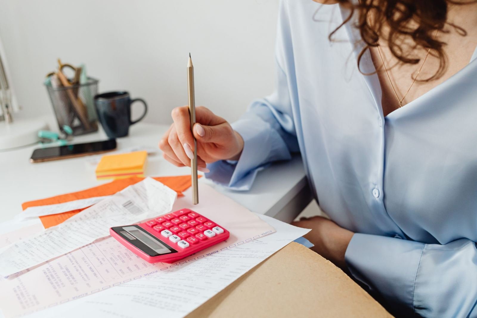 A person reviews paperwork at a desk using a pink calculator and pencil.