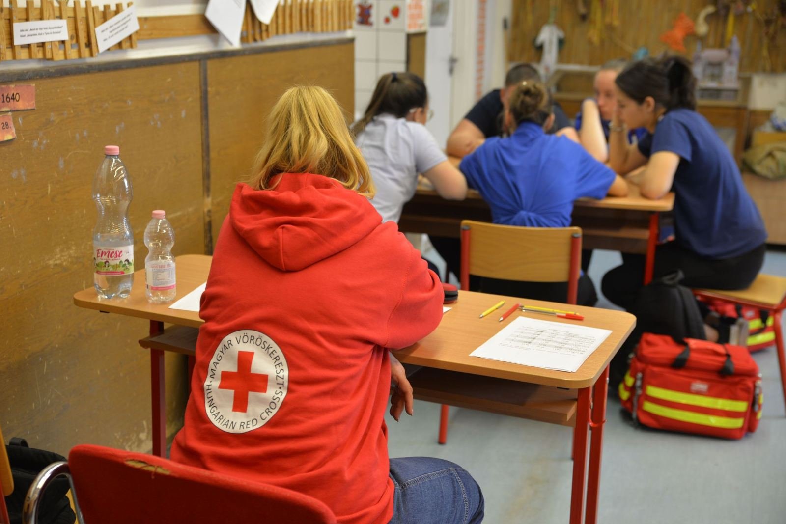 A person in a Red Cross hoodie sits at a desk with other students in a classroom