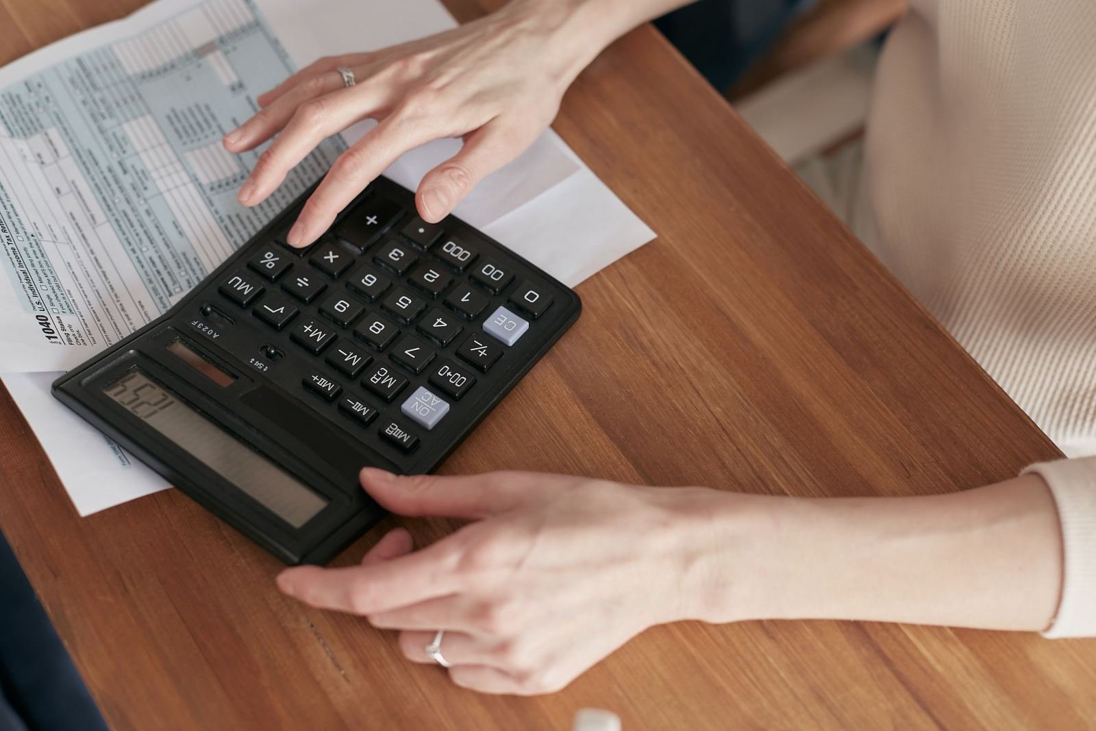 Hands using a calculator next to financial documents on a wooden desk