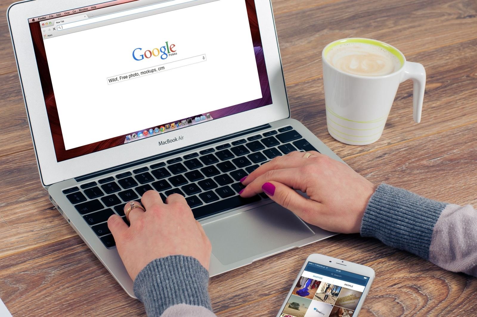 Hands typing on a laptop next to a cup of coffee and a smartphone