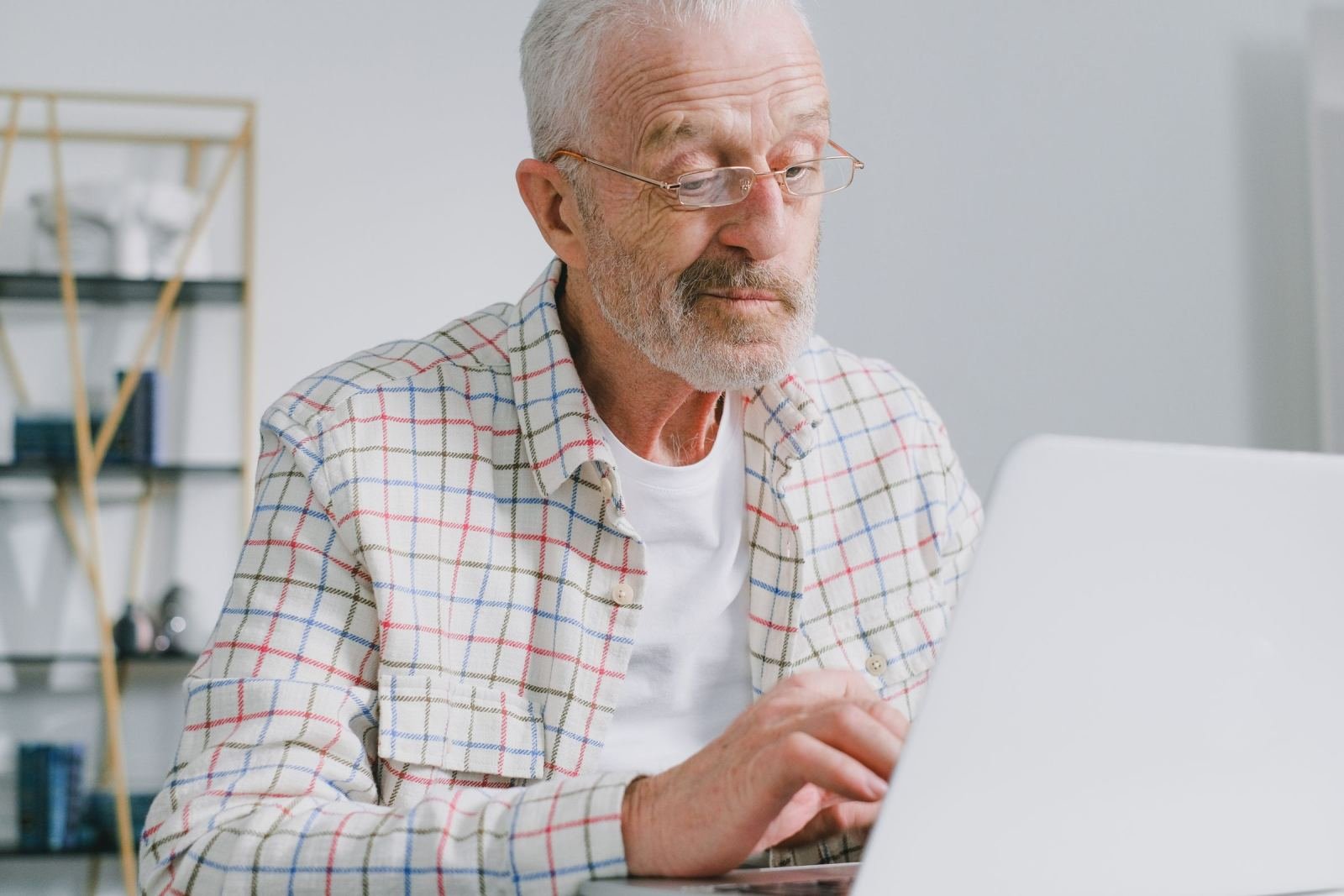 An older man with glasses uses a laptop at a desk