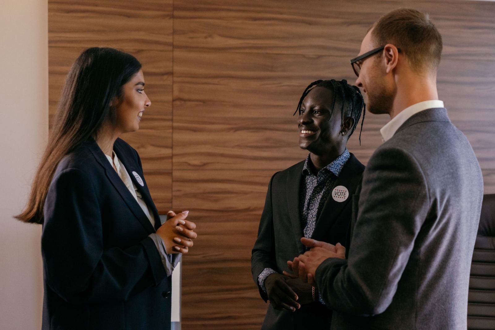 Three professionals in suits talking and smiling in an office