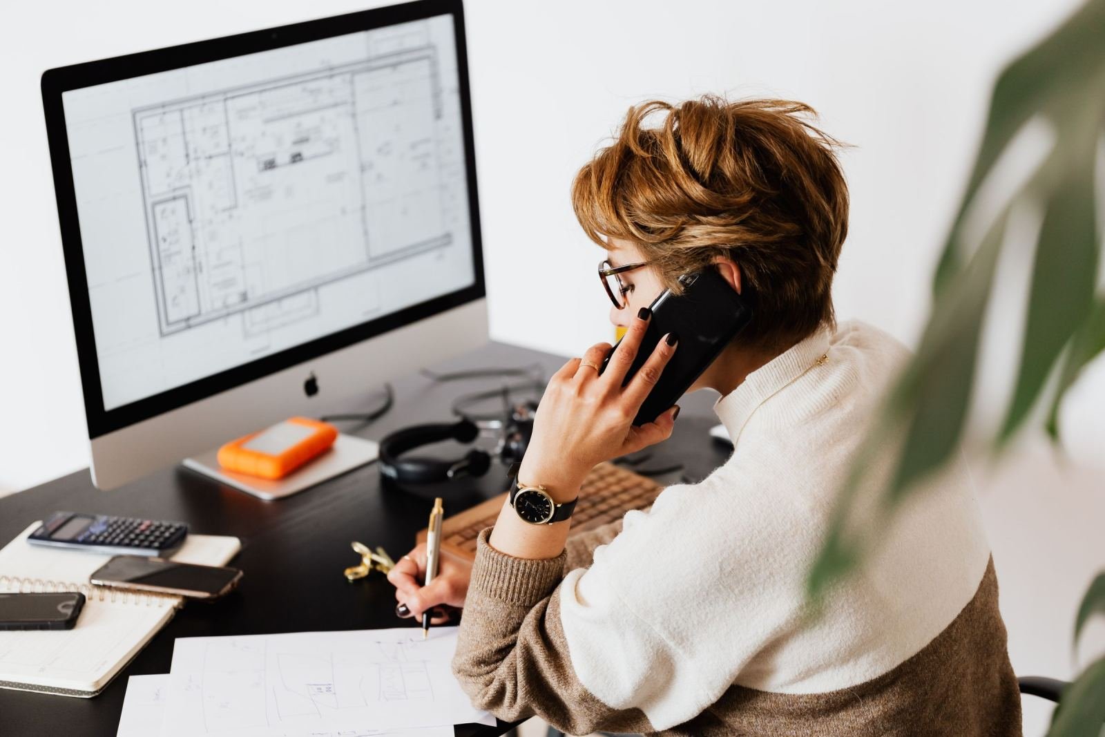 A woman on a phone call looks at a computer monitor in a bright office