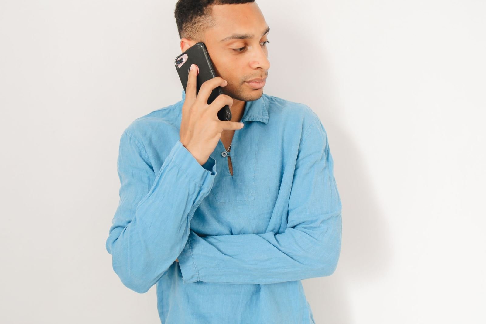 A man in a blue shirt talks on a black smartphone