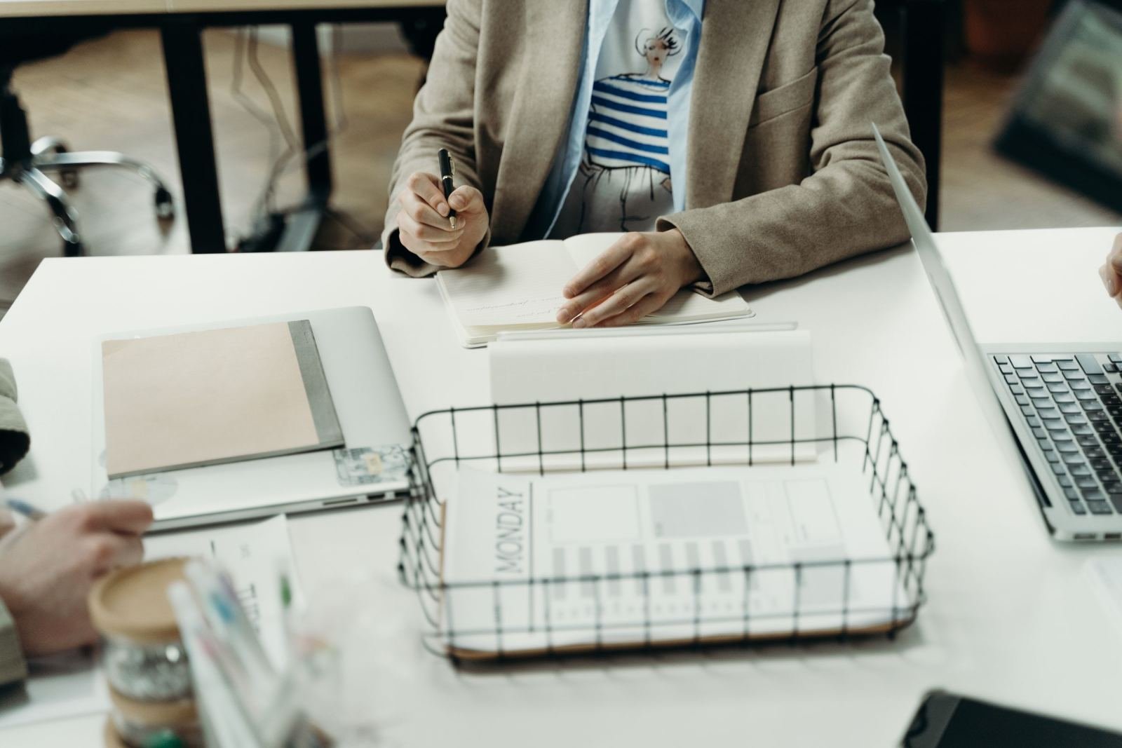 A person in a blazer sits at a desk with a notebook and laptop