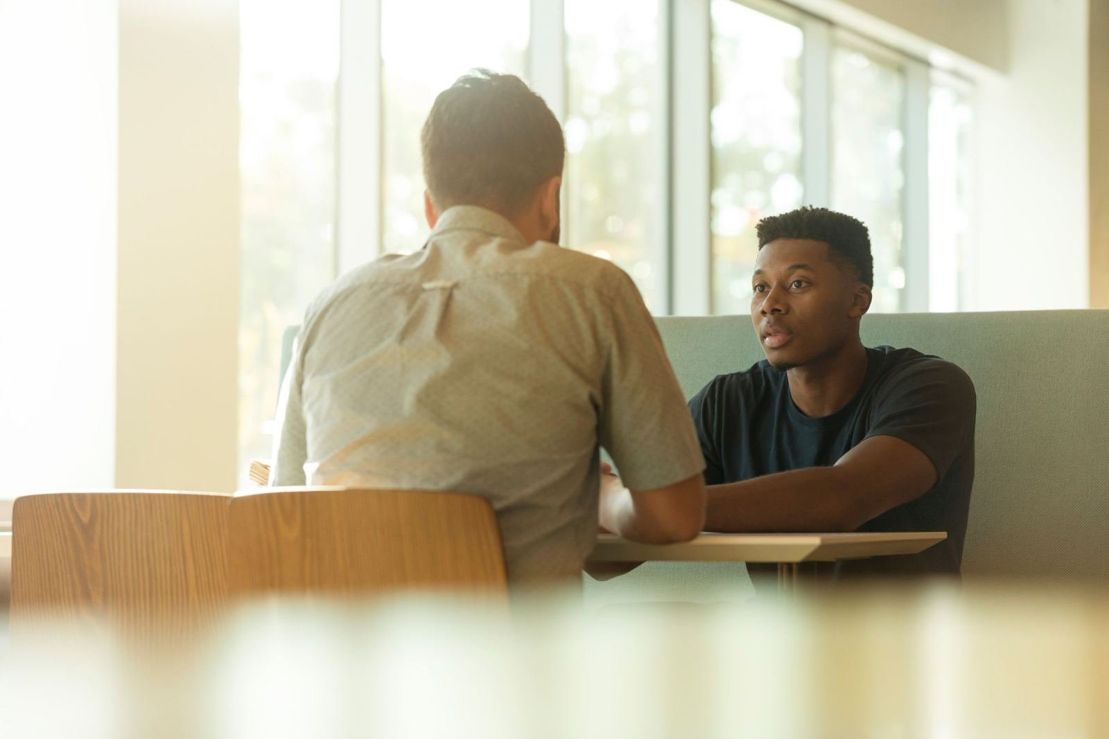 In a well-lit room, two men sit facing one another at a table.
