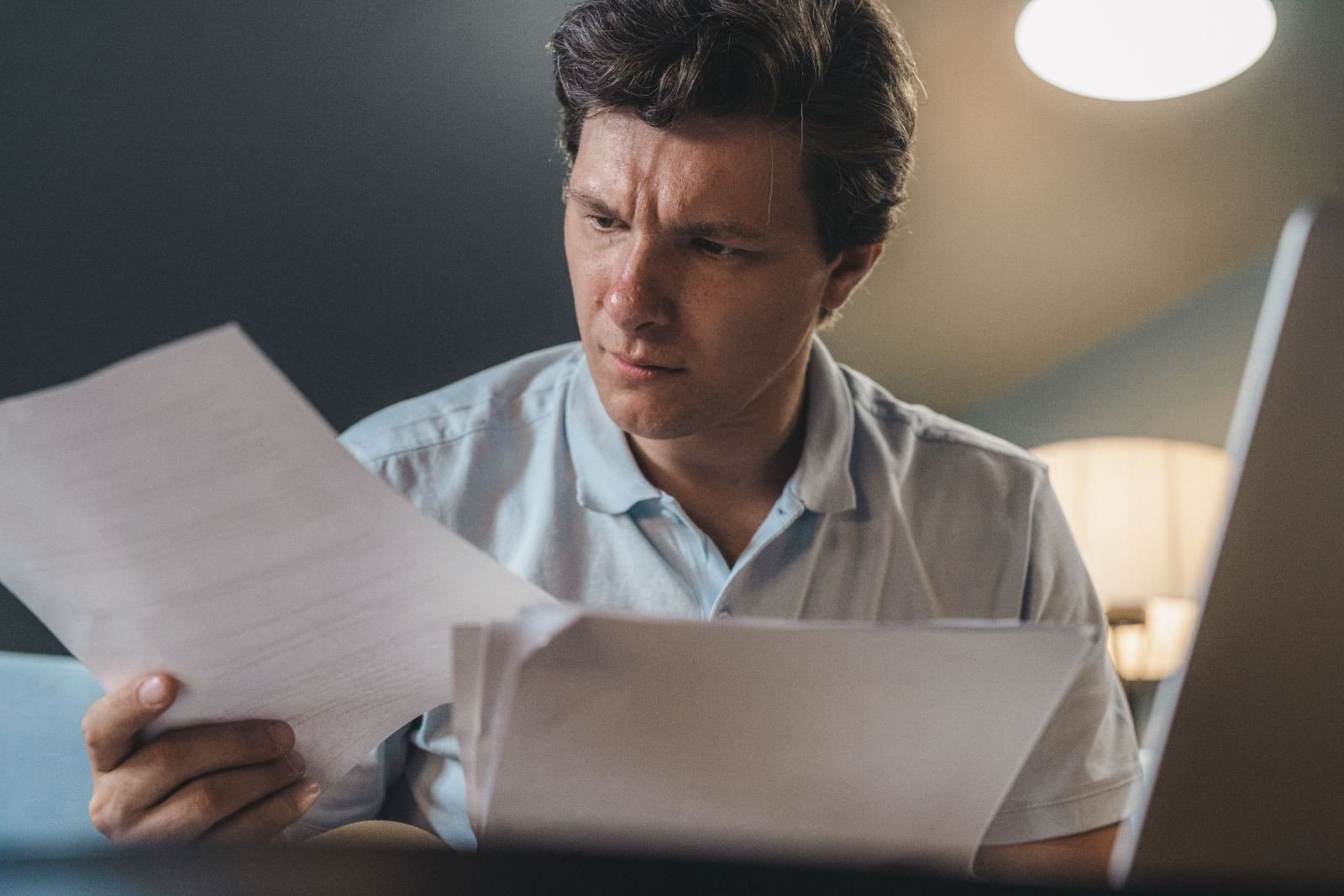 A man looks at a paper while sitting at a computer.