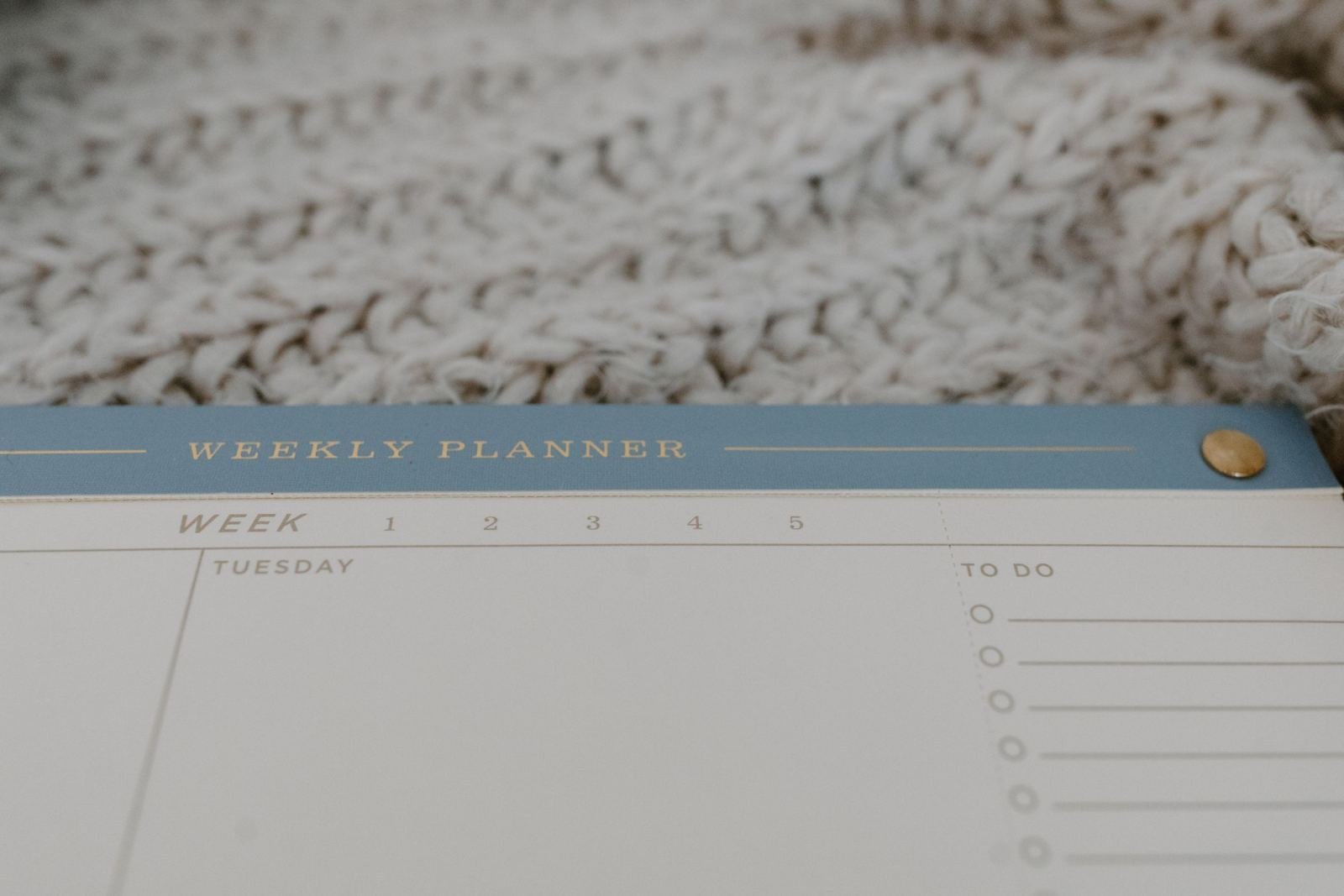 A weekly planner with a to-do list next to a white knitted blanket