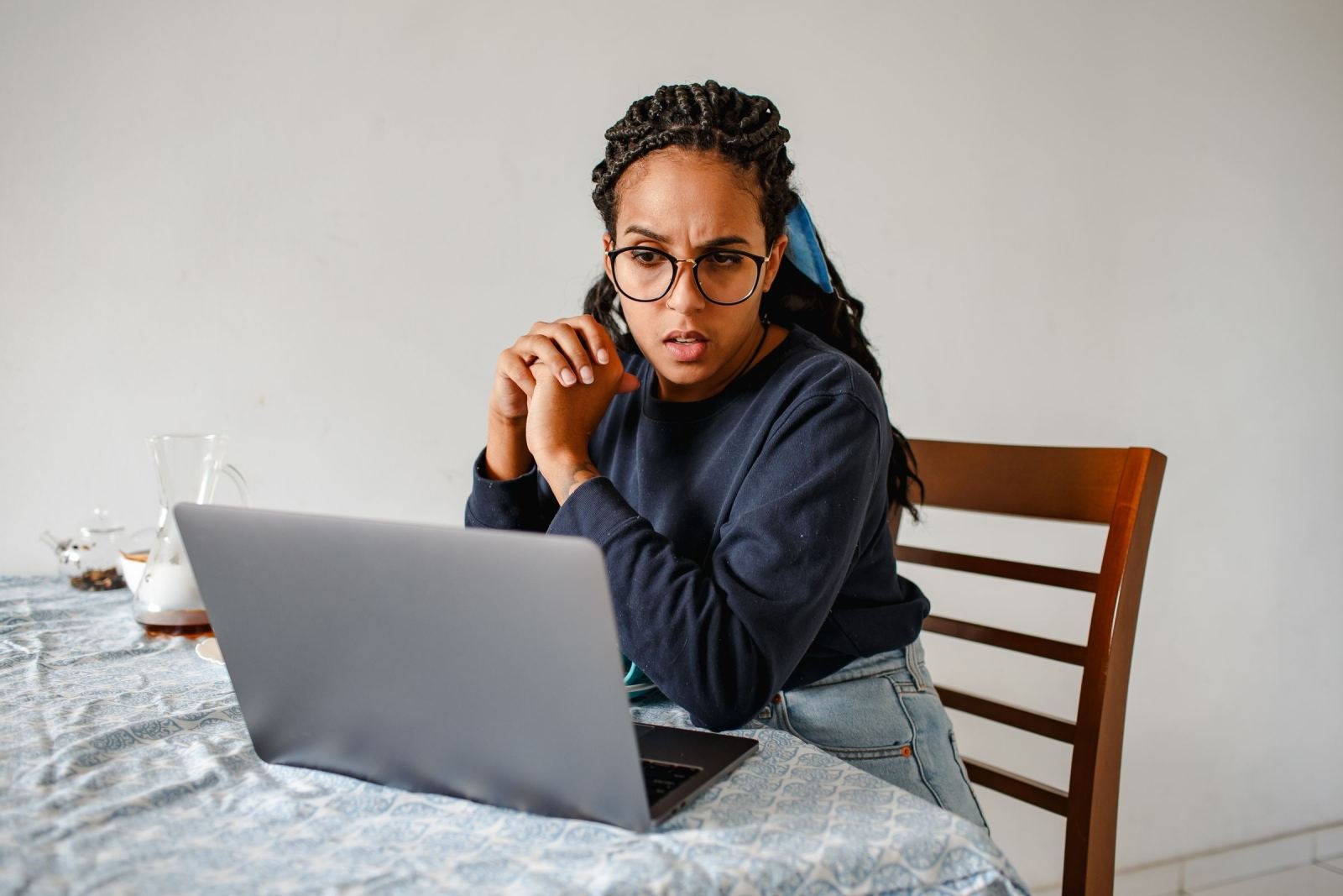 A woman wearing glasses looks worriedly at her laptop screen.