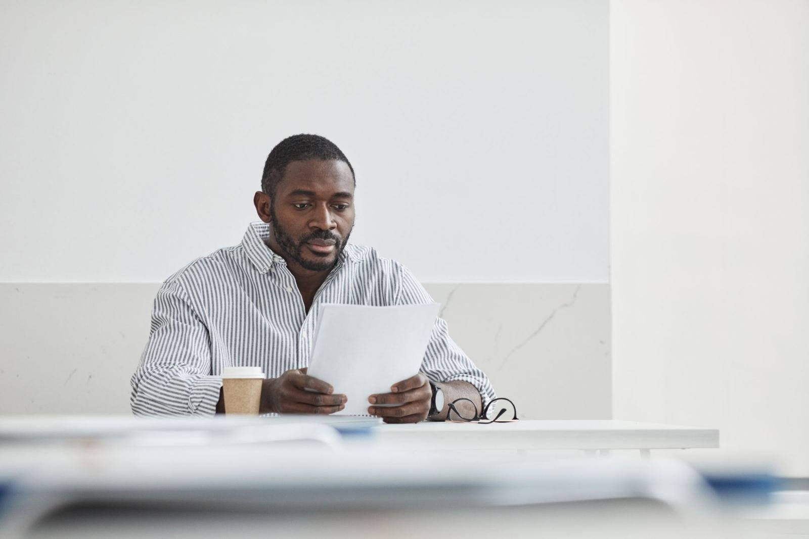 A man in a striped shirt reads a document at a white table