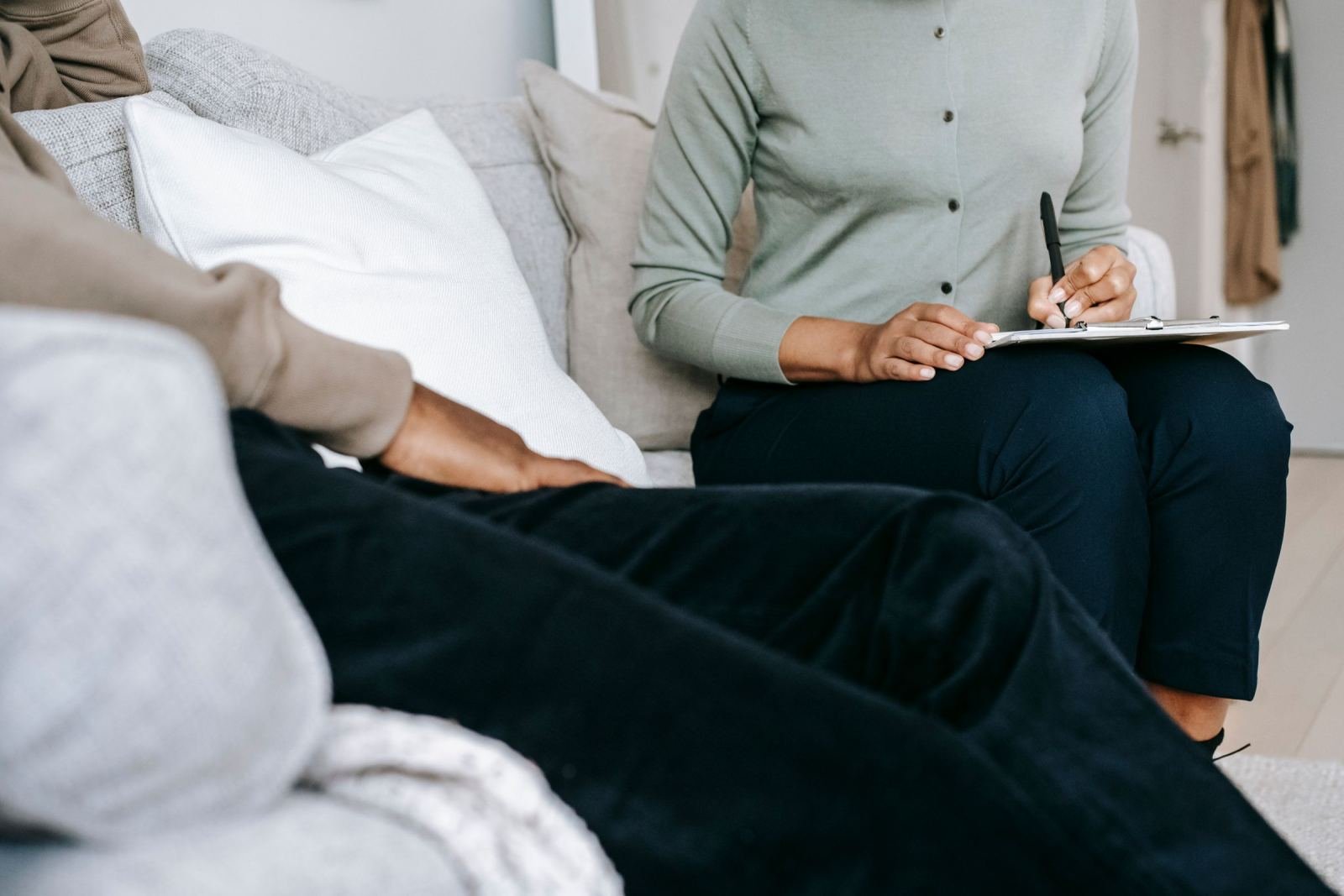 A person in a green shirt takes notes on a clipboard while sitting on a sofa with another person