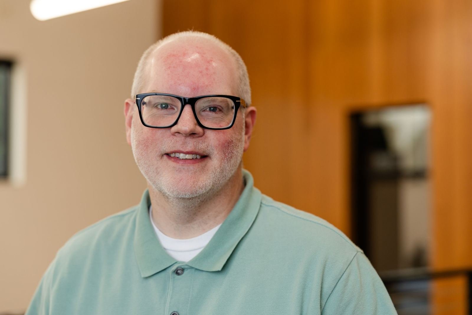 A smiling man with glasses wearing a light green polo shirt