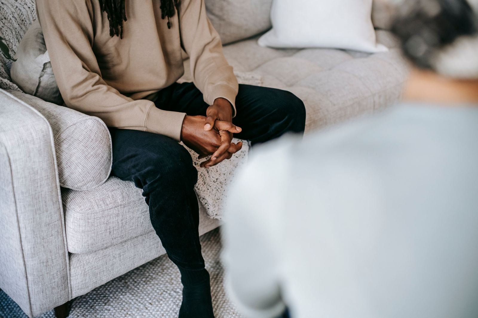 A person sits on a sofa with hands clasped while talking to someone