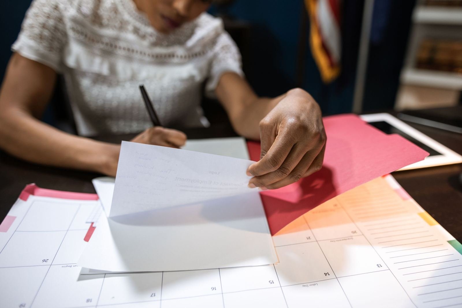 A person reviews a document over a calendar and a red folder at a desk