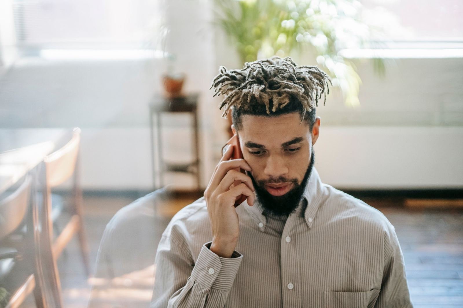 A man with dreadlocks speaks on a phone while looking down