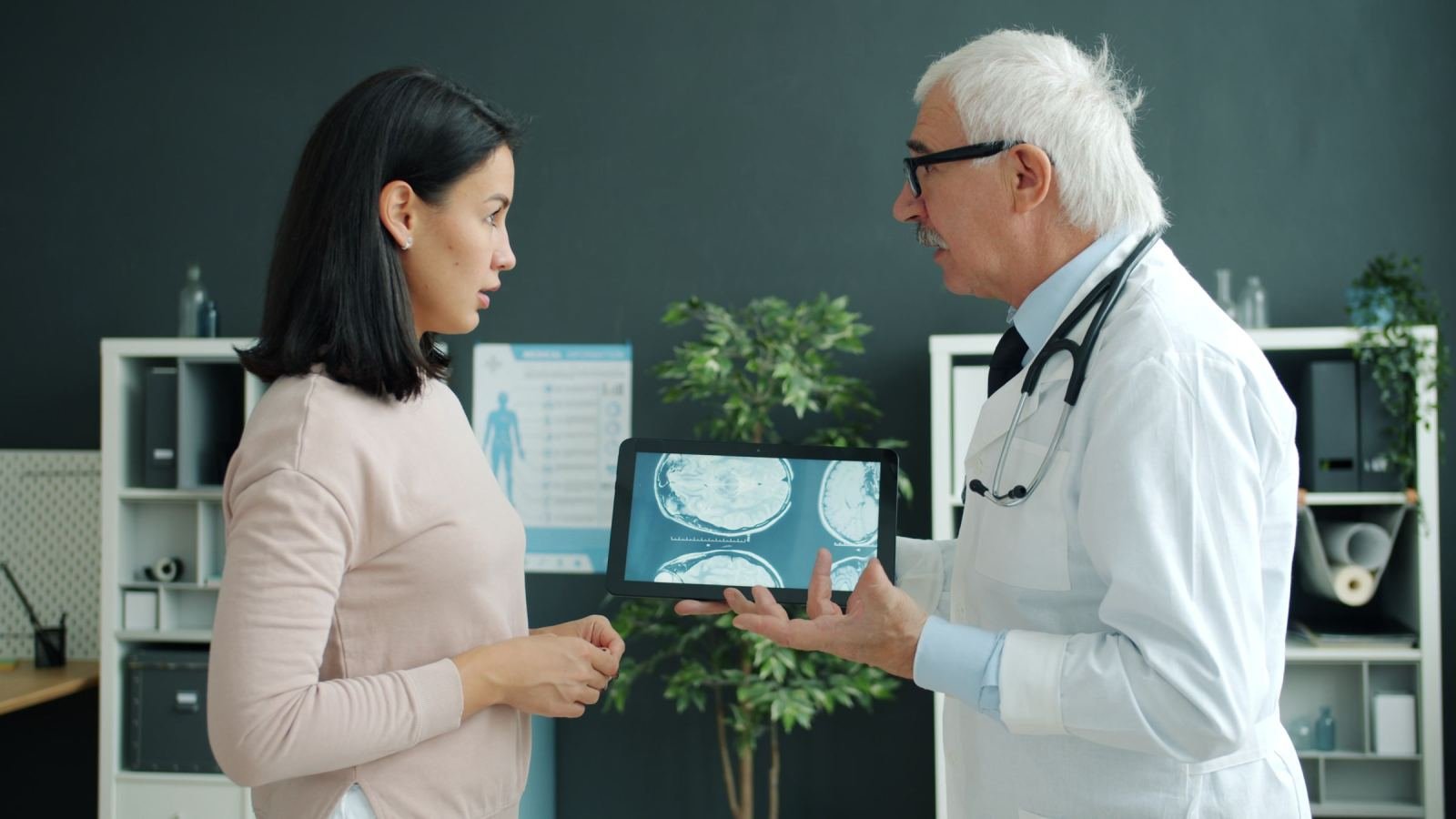 A doctor in a white coat shows brain scans on a tablet to a woman